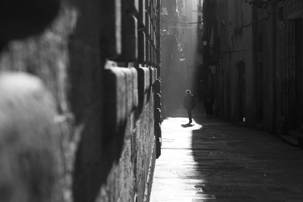 Silhouette of a person walking in a narrow, shadowed alley with dramatic sunlight.