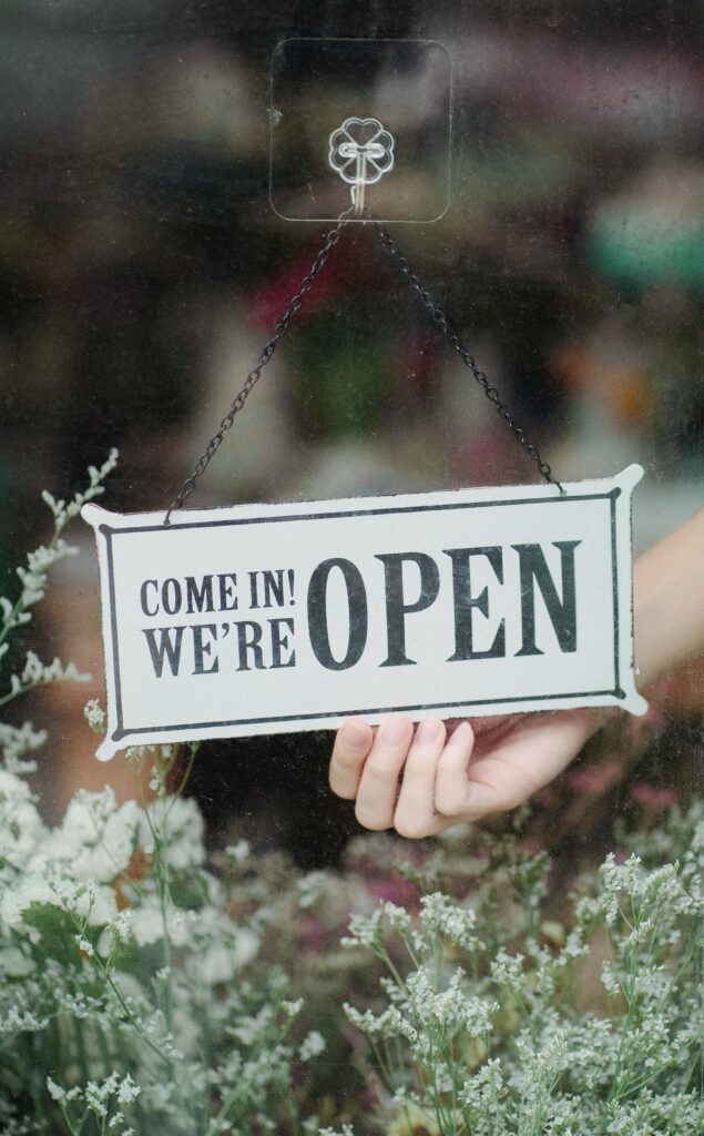 A welcoming open sign in a flower shop window with delicate blossoms in the foreground.